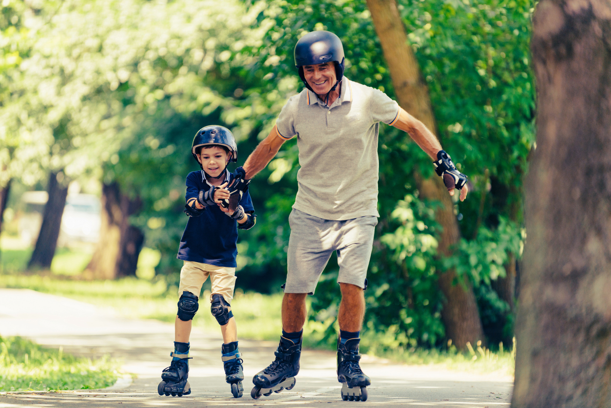 The image shows a young child and his grandfather roller skating outside. It represents how to ensure skating with your child is safe and fun.