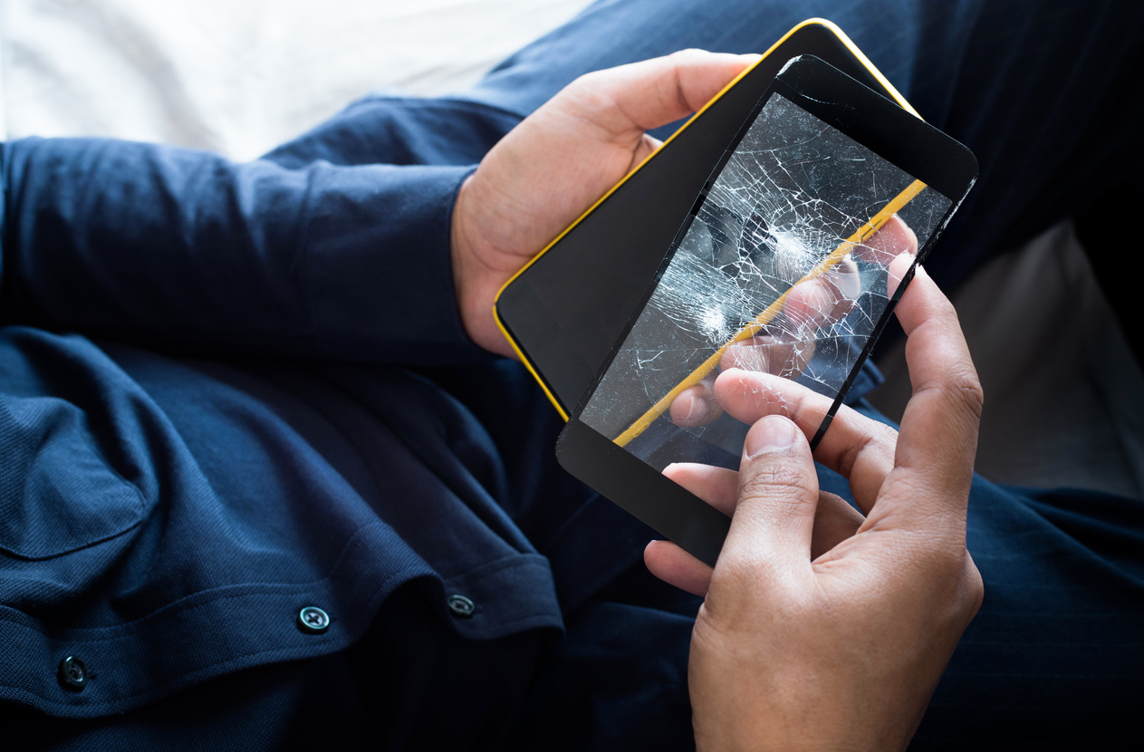 The image shows a male holding a cracked screen protector and unscratched phone in his hands to represent the reasons you should have a screen protector on your phone.