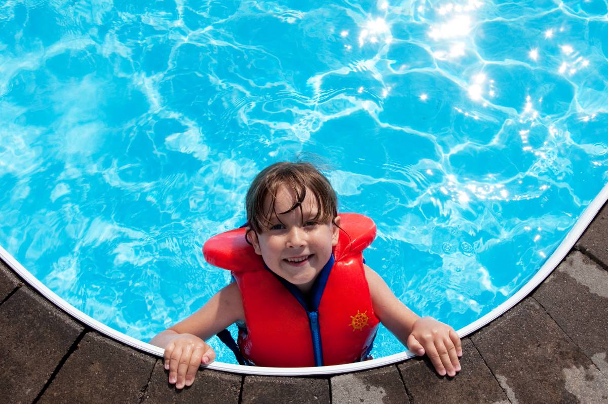Kid in life vest safely swimming in hotel pool.