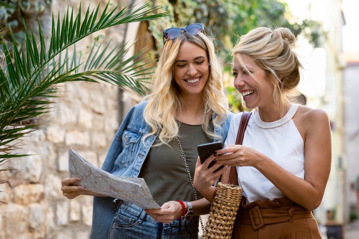 Two women using a phone and map to travel in the city.