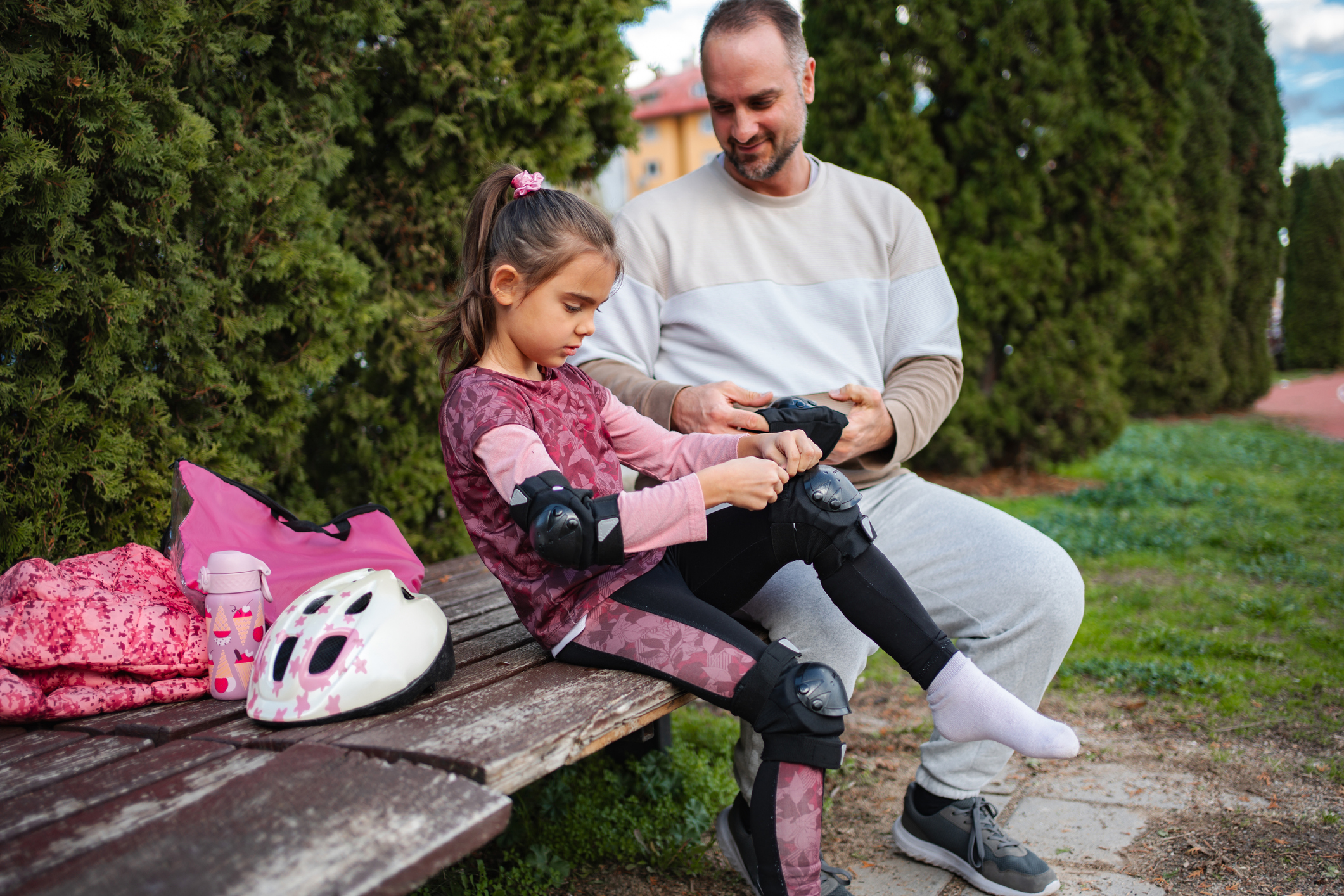 Father helping daughter put on safety gear for roller skating.