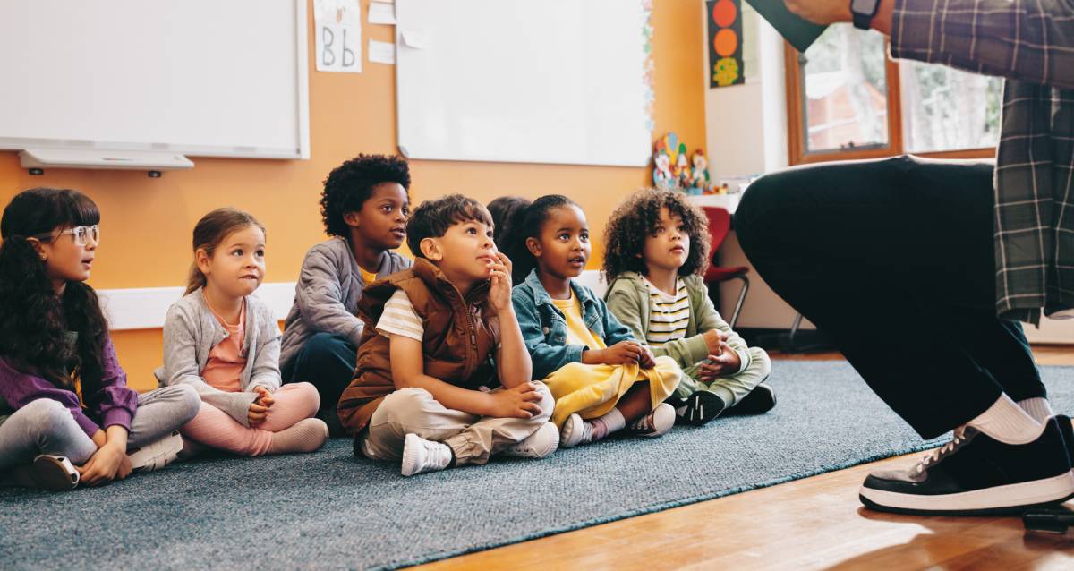 Students sit and listen to a story from their teacher.