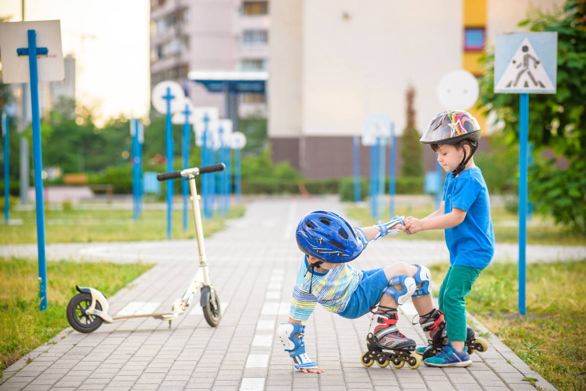 Two boys in park, playing with scooter and roller skates.