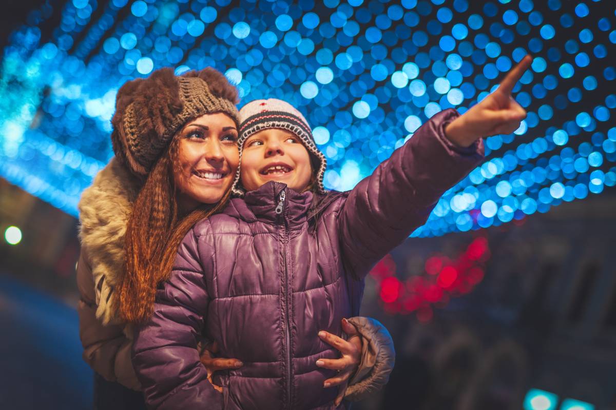 Cheerful young woman and her daughter are having fun in the city street at Christmas time.