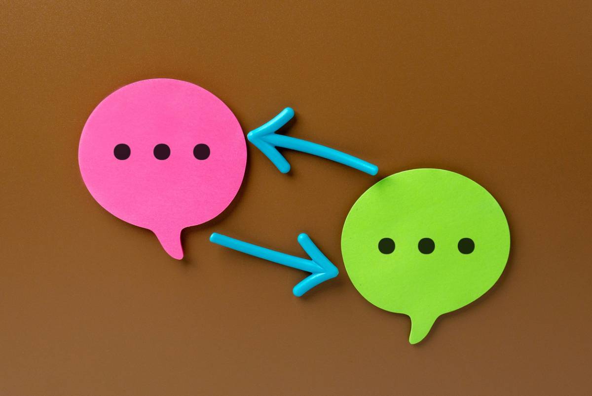 Pink and green speech bubbles are connected by two arrows. Feedback loop and iterative communication cycle concept.