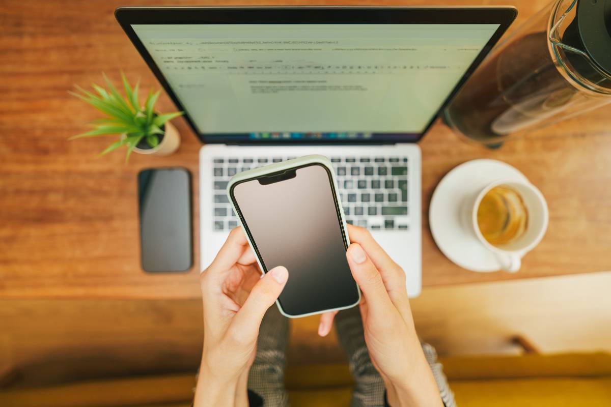 Image of hand holding phone with laptop in the background.