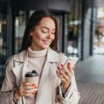 Woman smiling at phone and holding coffee.