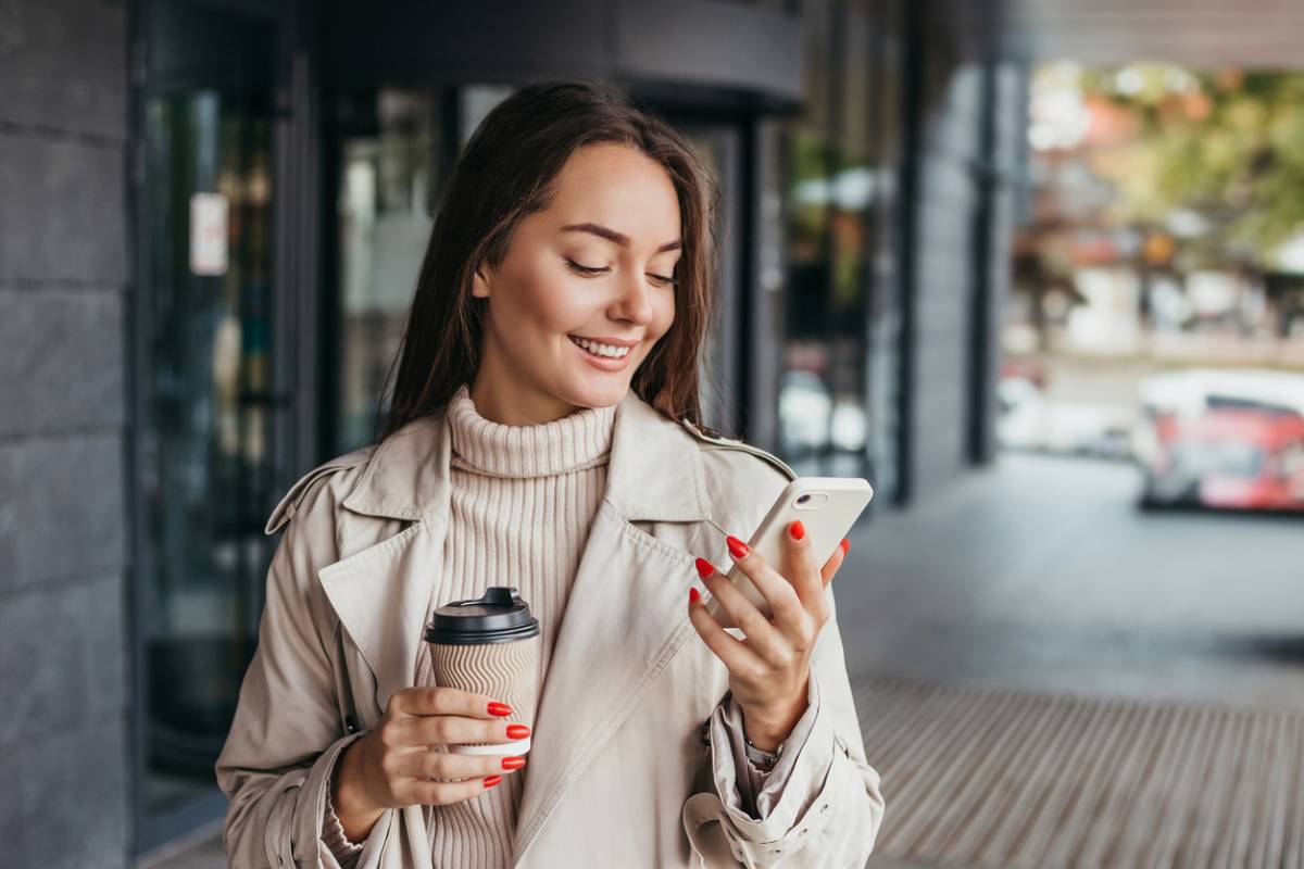 Woman smiling at phone and holding coffee.